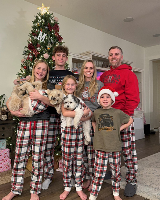 Dr. Caleb Goodman's family in matching plaid pajamas with dogs, posing in front of a Christmas tree.