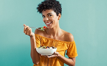Woman eating bowl of fruit while smiling