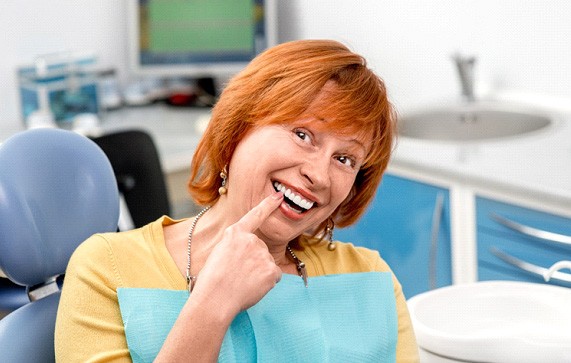 Senior woman in dental chair pointing to smile