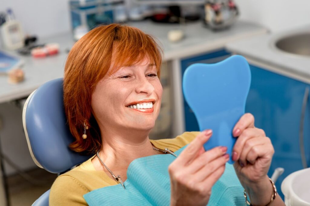 A woman looking in the mirror at her teeth at the dentist.