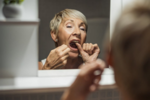 Women flossing her dental implants in the mirror